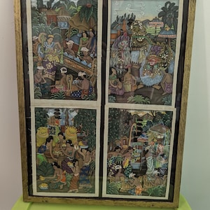 Può includere: Un'opera d'arte incorniciata con quattro pannelli con illustrazioni dettagliate e colorate della vita balinese. L'opera raffigura scene con figure in abiti tradizionali, ambientate in un paesaggio lussureggiante e templi. La cornice è di colore marrone chiaro.