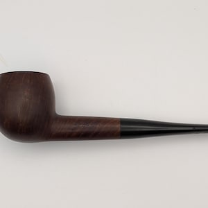 May include: A tobacco pipe featuring a smooth, dark brown wooden bowl with a visible grain pattern and a long, tapered black stem. The pipe has a classic, curved shape with a rounded bowl and a slender mouthpiece extending from the wooden shank.