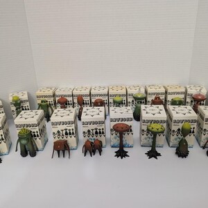 May include: A collection of small, stylized figurines and their boxes. The figurines are various colors and shapes, including mushroom-like and humanoid forms. The boxes are white with black and blue text and graphics.
