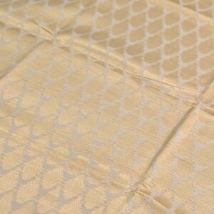 May include: A light beige fabric featuring a repeating pattern of white teardrop or petal shapes arranged in a grid. The material has a subtle sheen and a woven texture, with visible horizontal and vertical seams dividing the fabric into sections.