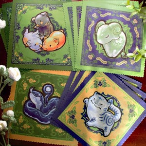 May include: Four colorful square fabric panels with green borders and intricate designs. Each panel features a different animal: a pig, a ram, a snake, and a cat. The animals are depicted in a cartoon style and are surrounded by floral patterns.