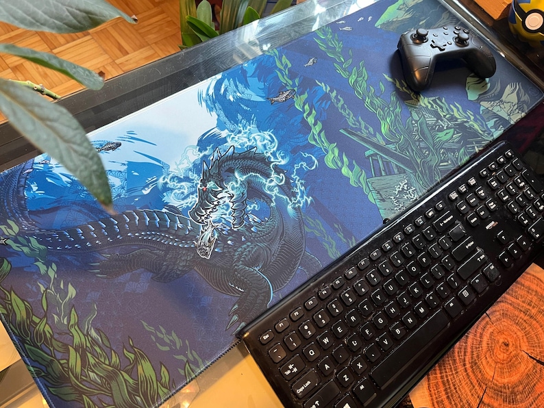 May include: A blue and green gaming mouse pad with a black sea monster illustration. The monster is surrounded by blue water and green seaweed. A black keyboard and a black game controller are on the mouse pad.