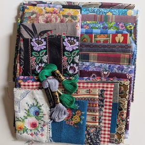 May include: A collection of assorted fabric scraps featuring various floral, plaid, gingham, and geometric patterns in multiple colours, stacked with two skeins of embroidery floss in green and light purple resting on top of the fabric pile.