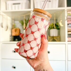 May include: A pink smoothie in a clear glass with a red heart pattern. The glass has a bamboo lid and a straw.