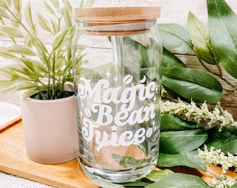 May include: A clear glass jar with a bamboo lid and a straw. The jar has a white vinyl decal that says "Magic Bean Juice".