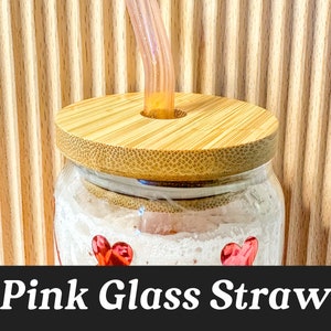 May include: A glass jar with a bamboo lid and a pink glass straw sticking out of the lid. The jar has a white background with red hearts.