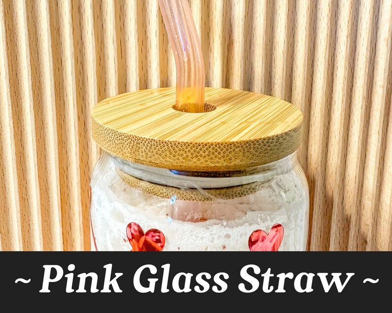 May include: A glass jar with a bamboo lid and a pink glass straw sticking out of the lid. The jar has a white background with red hearts.