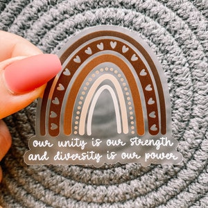 May include: A clear sticker with a rainbow design in shades of brown and beige. The rainbow has small hearts around the edges and a dotted pattern. The sticker has the text "our unity is our strength and diversity is our power" in white.