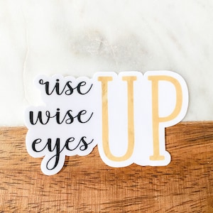 May include: White sticker with black text that reads "rise wise eyes up" with the word "up" in gold.