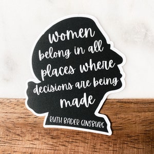 May include: Black and white sticker with a silhouette of a woman's head and the quote "Women belong in all places where decisions are being made" by Ruth Bader Ginsburg.