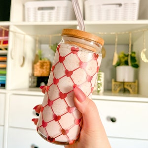 May include: A glass jar with a pink smoothie and a clear straw. The jar has a wooden lid and a pink and white heart pattern.