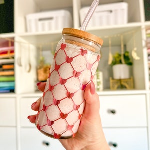 May include: A glass jar with a pink smoothie and a clear straw. The jar has a wooden lid and is decorated with a red heart pattern.