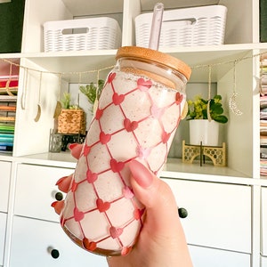 May include: A pink smoothie in a clear glass bottle with a bamboo lid and a clear straw. The bottle has a pink and white heart pattern.