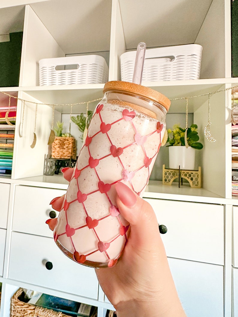 May include: A pink smoothie in a clear glass bottle with a bamboo lid and a clear straw. The bottle has a pink and white heart pattern.