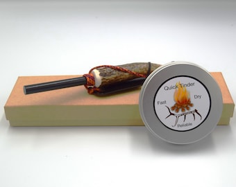 May include: A set of fire starting tools in a brown box. The tools include a black fire starter and a small tin of tinder. The tin has a label that says "Quick Tinder" and lists the qualities of the tinder as "Fast", "Dry", and "Reliable".