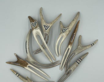 May include: A collection of eight hair forks crafted from natural antler material. Each piece features a unique bifurcated design with smooth, tapered prongs. Several forks are decorated with etched geometric patterns, including chevrons and stripes.