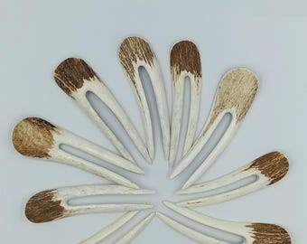 May include: A collection of eight hair forks arranged in a circular pattern. Each fork has a light-colored, elongated body with a U-shaped opening and a brown, textured top. The forks are made of a natural material.