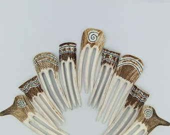 May include: A collection of handcrafted hair combs. The combs feature a light brown and white color scheme with decorative patterns and spiral designs. The combs are arranged in a fan shape against a white background.