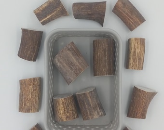 May include: A gray plastic rectangular basket containing four cylindrical brown antler segments, surrounded by nine additional antler segments arranged in a circular pattern around the basket on a plain white surface.