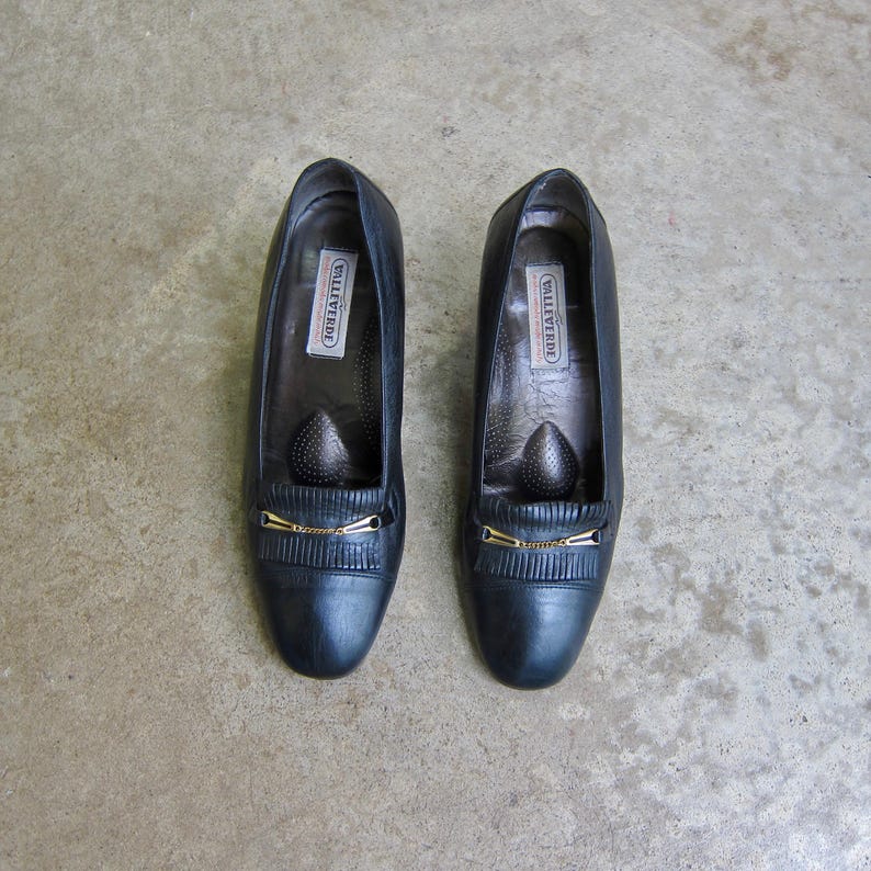 May include: A pair of black leather shoes with gold buckles and the word "Willaert" printed on the inside of each shoe.