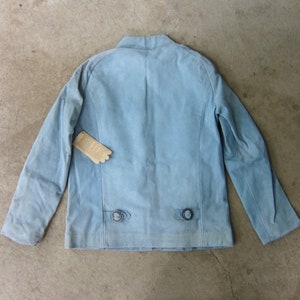 May include: A light blue denim jacket with a stand-up collar and two button closures on the back.