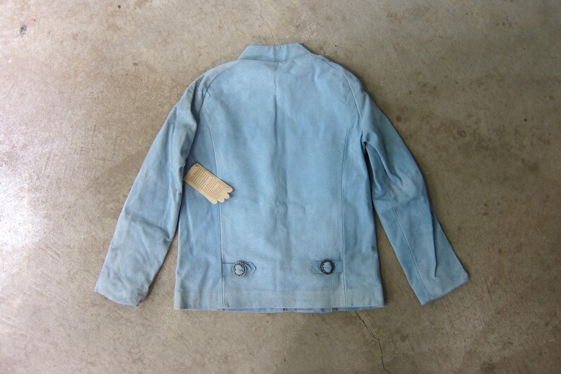 May include: A light blue denim jacket with a stand-up collar and two button closures on the back.