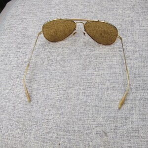 Puede incluir: Gafas de sol aviador con montura dorada y lentes marrones. Las gafas tienen un doble puente y patillas curvas. Las lentes son de color marr&oacute;n c&aacute;lido y las monturas tienen un acabado dorado brillante.