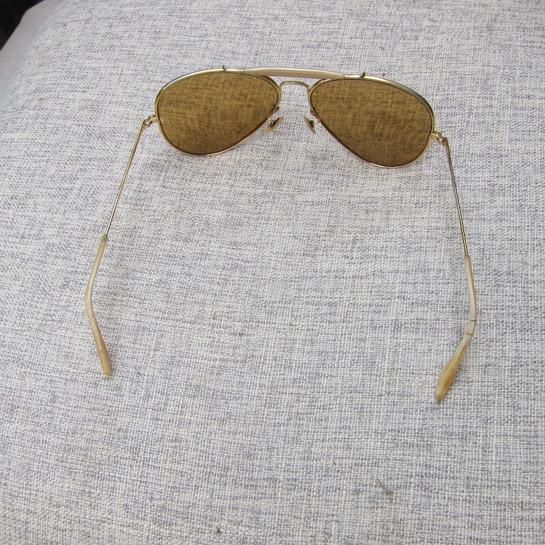 Puede incluir: Gafas de sol aviador con montura dorada y lentes marrones. Las gafas tienen un doble puente y patillas curvas. Las lentes son de color marr&oacute;n c&aacute;lido y las monturas tienen un acabado dorado brillante.