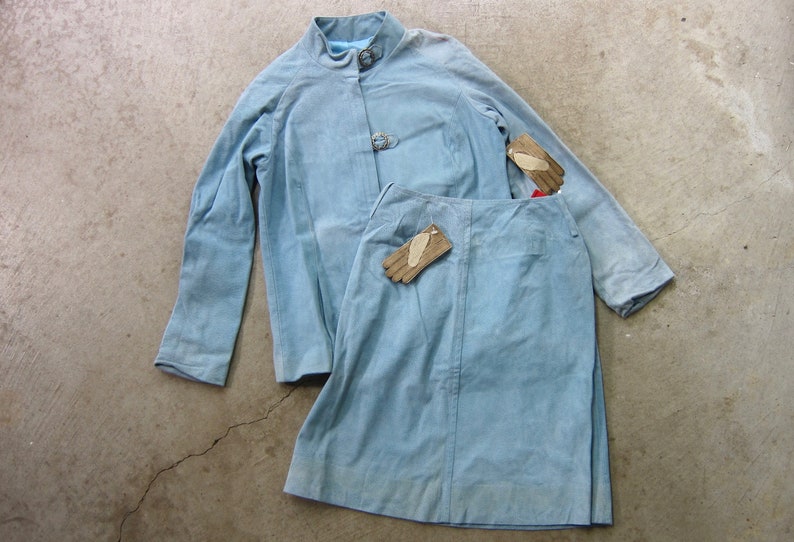 May include: A light blue suede jacket and skirt set with two pairs of brown leather gloves.