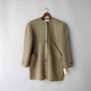 May include: A beige long-sleeved jacket with a button closure and two pockets. The jacket has a tag attached to the bottom right side.