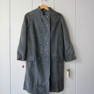 Peut inclure: Un long manteau en daim gris fonc&eacute; avec un col mandarin et une fermeture &agrave; double boutonnage. Le manteau a six boutons argent&eacute;s et deux poches.