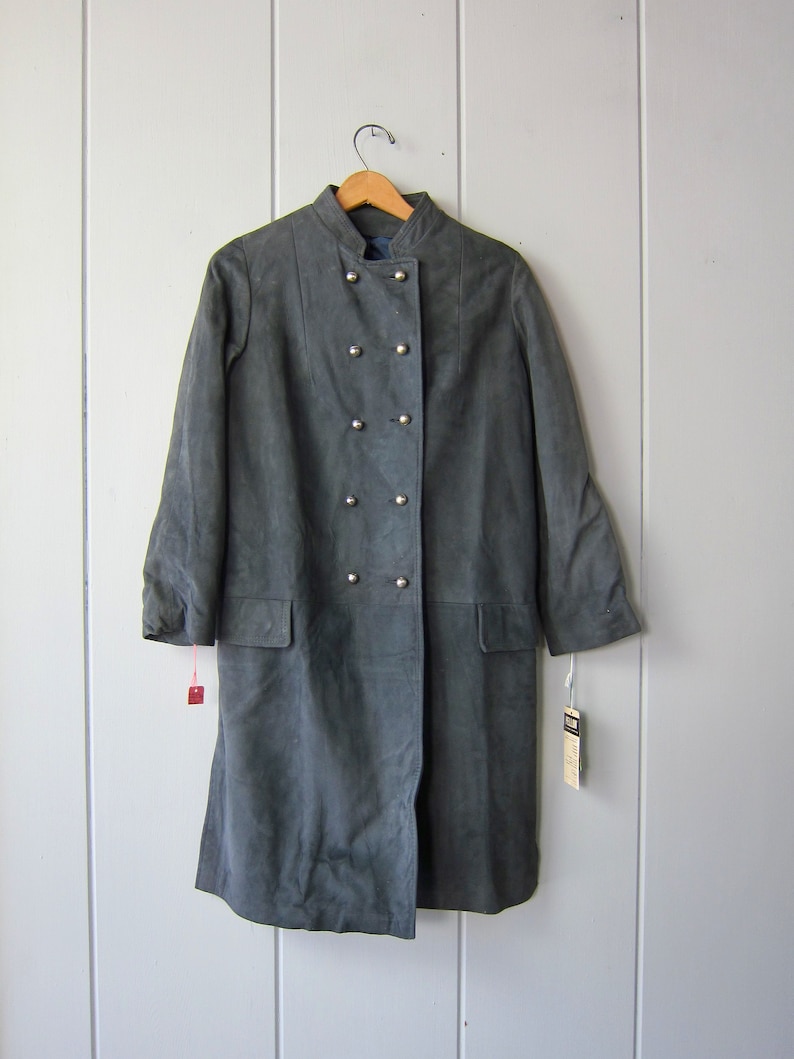 Peut inclure: Un long manteau en daim gris fonc&eacute; avec un col mandarin et une fermeture &agrave; double boutonnage. Le manteau a six boutons argent&eacute;s et deux poches.
