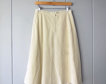 Könnte beinhalten: Ein Vintage-Rock mit hoher Taille in einem cremefarbenen und hellgrünen Chevron-Muster. Der Rock hängt an einem Holzbügel vor einem grauen Hintergrund. Der Rock hat einen Knopfverschluss an der Taille.