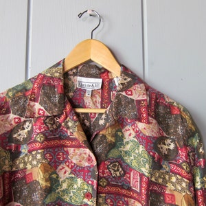May include: A button-down shirt with a colorful patchwork pattern in shades of red, brown, green, and gold. The shirt is hanging on a wooden hanger. The label reads "Christie & Jill".