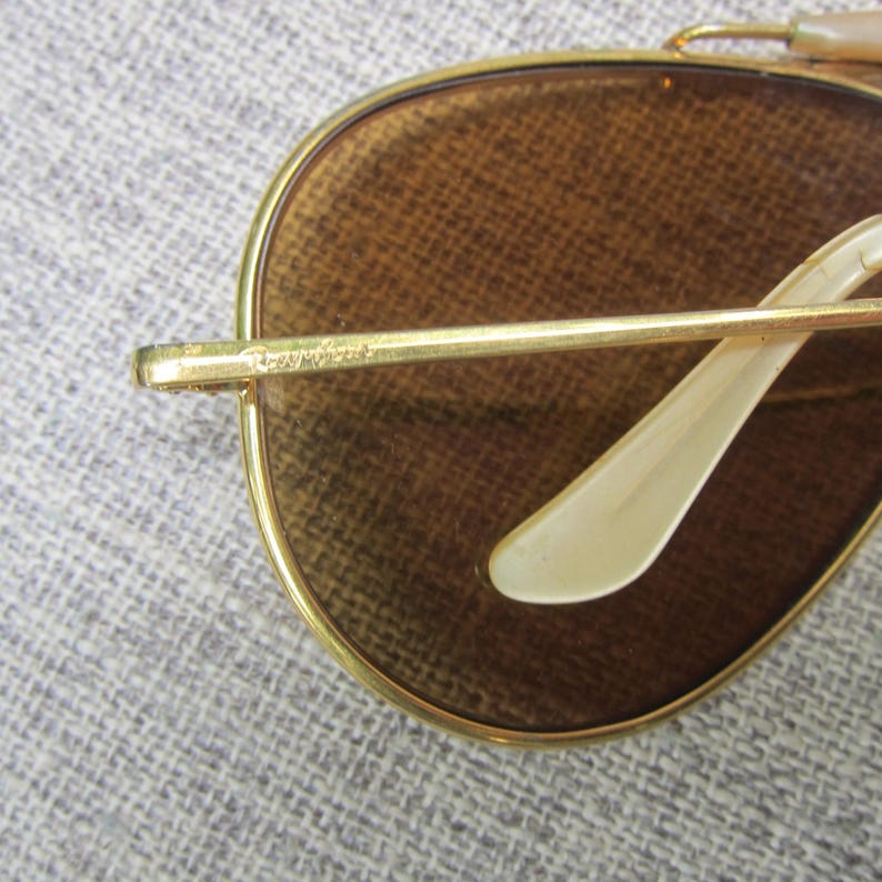 Puede incluir: Primer plano de gafas de sol con montura dorada y lentes marrones. Las gafas de sol tienen una forma de aviador cl&aacute;sica, con montura dorada y patillas de color marr&oacute;n claro. Las lentes son de color marr&oacute;n c&aacute;lido.