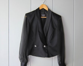 May include: A black blazer with sheer sleeves and a double-breasted closure. The blazer has two decorative buttons with rhinestones. The label reads "J.F. NYTES COLLECTION".