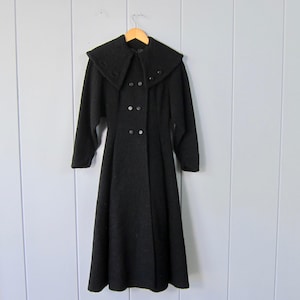 May include: A black wool coat with a large collar and a double breasted closure. The coat has a flared skirt and long sleeves.