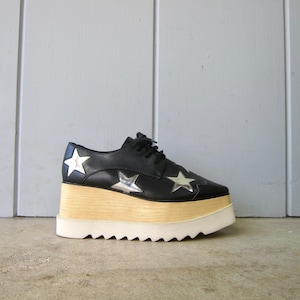 May include: Black leather platform shoes with silver star accents and a white platform sole.