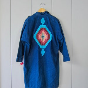 May include: A blue denim shirt with a geometric design on the back. The design is in shades of red, orange, and turquoise.
