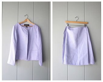 Può includere: Un tailleur gonna in lino lavanda con una chiusura a bottone singolo sulla giacca. La gonna è a trapezio e la giacca ha una tasca su ogni lato.