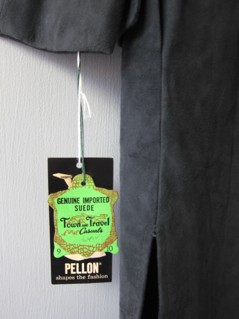 Peut inclure: Une &eacute;tiquette verte avec le texte "Genuine Imported Suede Town and Travel Casuals" et les num&eacute;ros "9" et "10" de chaque c&ocirc;t&eacute;. L'&eacute;tiquette est attach&eacute;e &agrave; une jupe en daim noir avec une fente dans le dos. L'&eacute;tiquette porte &eacute;galement le texte "Pellon shapes the fashion" en bas.