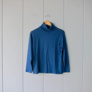 Op de afbeelding: Een blauwe trui met lange mouwen en een rolkraag.