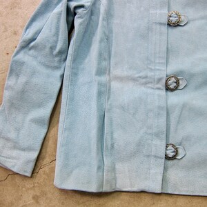 May include: A light blue jacket with long sleeves and three decorative buttons.