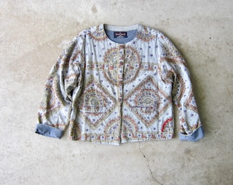 May include: A grey jacket with a paisley pattern and a button fastening. The jacket has a small red label on the collar that says "Sandalwood".