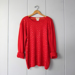 May include: Red sweater with a sparkly design. The sweater has a round neckline and long sleeves.