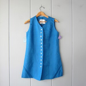 May include: A sleeveless blue linen dress with a button-up front and a slightly flared skirt.