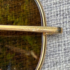 Puede incluir: Primer plano de gafas de sol con montura dorada y lentes marrones. La montura es de estilo aviador cl&aacute;sico, con una fina montura de metal dorado. Las lentes son de color marr&oacute;n oscuro, y el aspecto general es vintage y elegante.