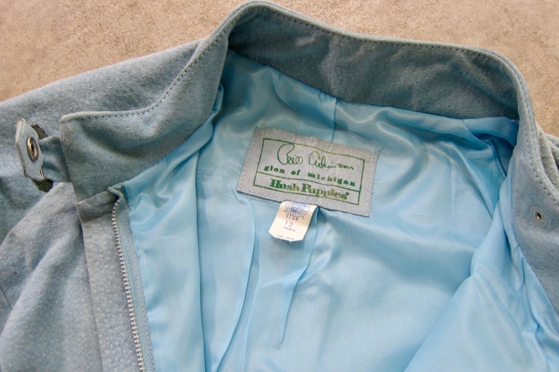 May include: A light blue suede jacket with a zip fastening and a Hush Puppies label. The label reads "Glen of Michigan Hush Puppies".