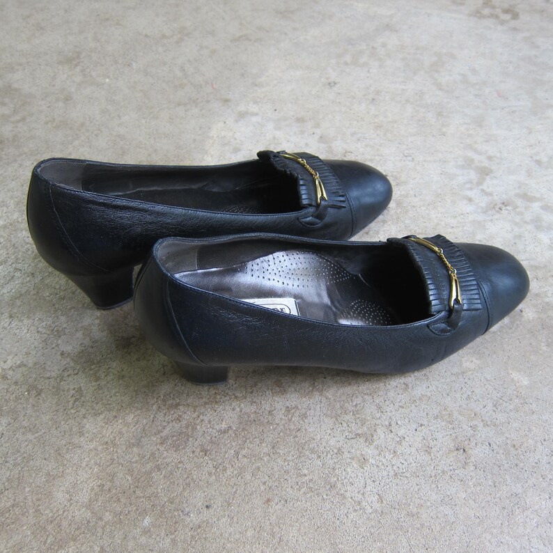 May include: A pair of black leather heeled shoes with a gold buckle and fringe detail.