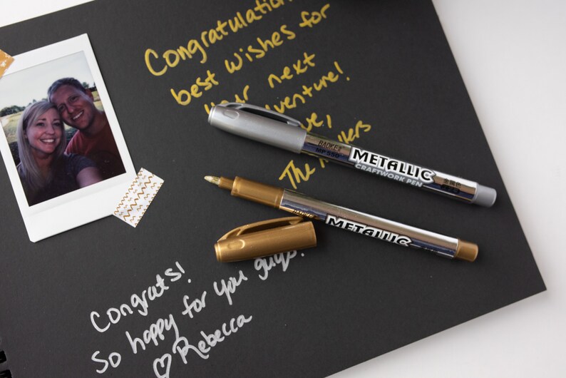 May include: Two metallic markers, one gold and one silver, on a black surface. The markers are labeled "Metallic Craftwork Pen". The text "Congrats! So happy for you guys. Rebecca" is written in white on the surface.